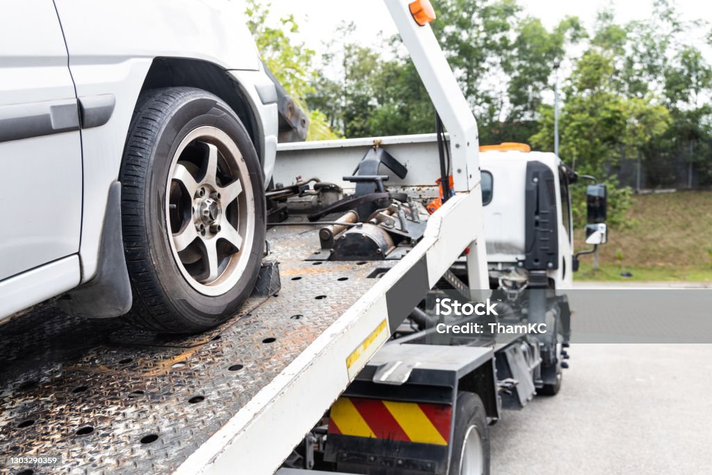 Cable attached to broken down car being pulled onto flatbed tow truck